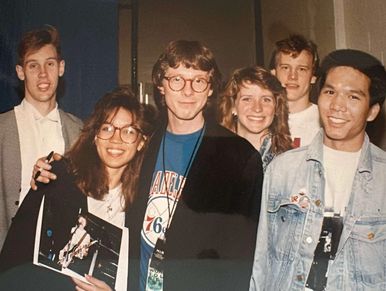 A group of six young adults smiling in a casual indoor setting.