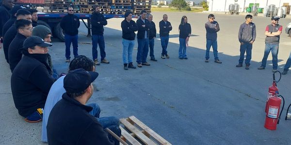 Workers gather outdoors for a safety briefing with fire extinguishers visible.