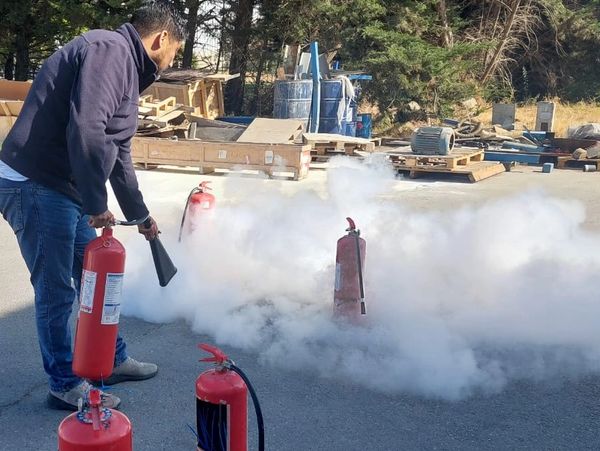 Man practicing fire extinguisher use outdoors with multiple extinguishers.