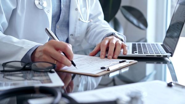 Doctor man wearing whit medical coat over a blue shirt is writing medical records