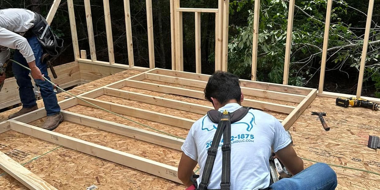 Two workers framing a wooden structure at a construction site outdoors.