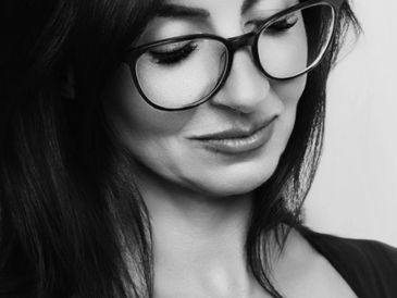 Woman with glasses looking down and smiling gently.