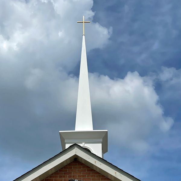 White church steeple with a gold cross against a cloudy sky.