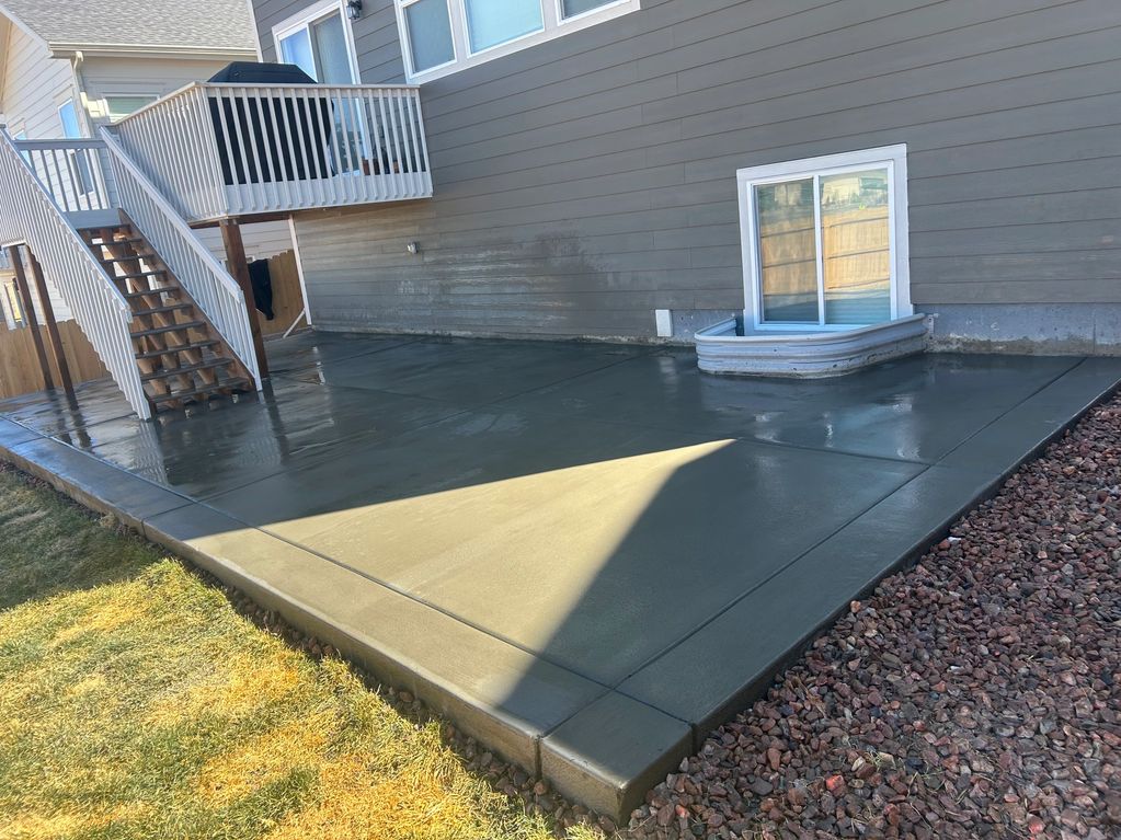 Freshly poured and smoothed concrete patio outside a house with stairs and window well.