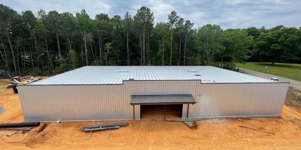 Large metal building under construction surrounded by trees and dirt.