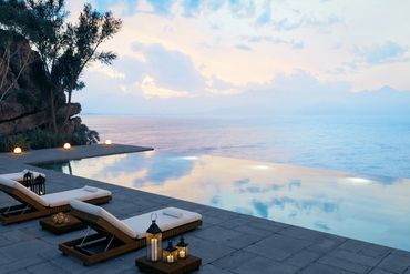 Chic poolside loungers with candle lanterns overlooking an infinity pool and ocean at sunset.