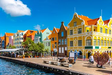 Colorful Dutch colonial buildings along a waterfront promenade under a clear blue sky.