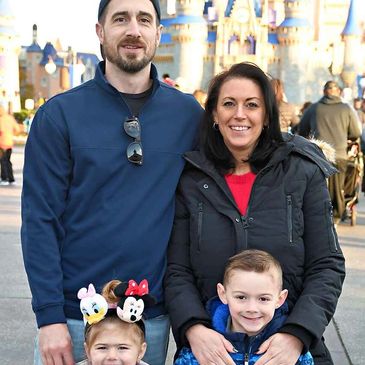 Family of four posing happily in front of a castle at a theme park.
