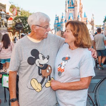 Elderly couple wearing Mickey and Minnie shirts at a theme park.