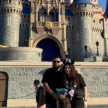 A family posing happily in front of a castle at a theme park.
