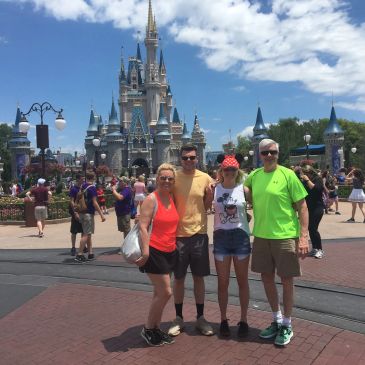 Family posing in front of Cinderella Castle at Disney World on a sunny day.