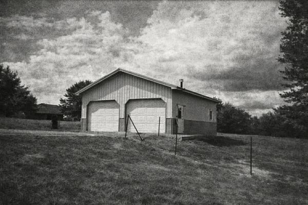 Black and white image of a detached garage in a grassy yard.