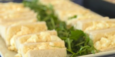 Close-up of egg salad sandwiches garnished with fresh greens on a platter.