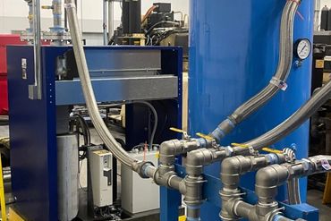 Industrial machinery with blue tanks and metal piping in a factory setting.