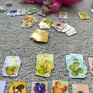 Child playing a colorful fruit-themed card game on a carpet.