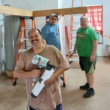 Three men working on a construction project indoors, one holding a nail gun.