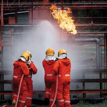 Firefighters in orange suits extinguishing a fire at an industrial site.