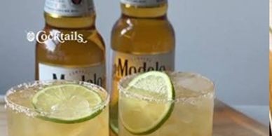 Two cocktails with lime and salted rims with beer bottles in the background.