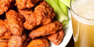 Plate of buffalo wings with celery and a glass of beer.