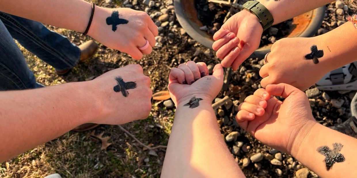 Hands with black X marks in a circle outdoors.