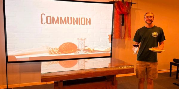 Man holding communion elements in front of a communion sign.