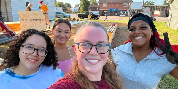 Group of four smiling women taking a selfie outdoors.
