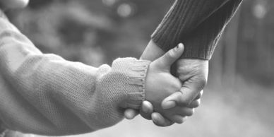Close-up of adult and child holding hands in black and white.