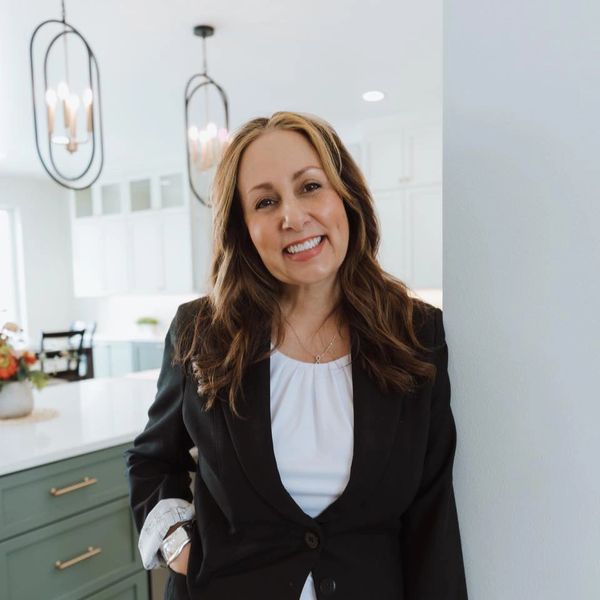 Smiling woman in a black blazer standing in a modern kitchen.