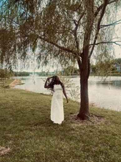 Woman in a white dress standing under a tree by a river.