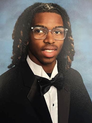 Young man in a formal tuxedo with glasses and styled hair.