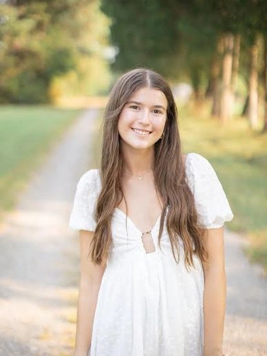 Young woman in white dress smiling outdoors on a sunny day.