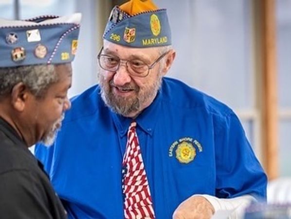 Two veterans in uniform caps engaged in conversation.