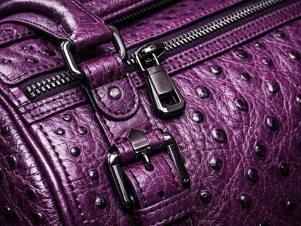 Close-up of a purple textured leather bag with zipper and buckle.