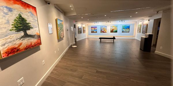 A spacious art gallery with paintings on the walls and wooden flooring.