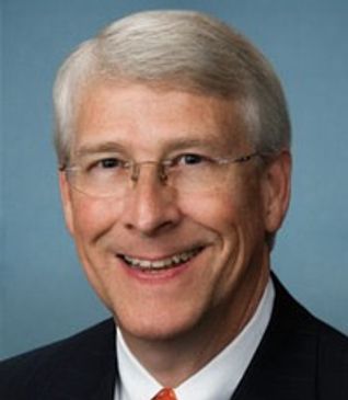 Smiling elderly man with glasses and white hair in a suit.