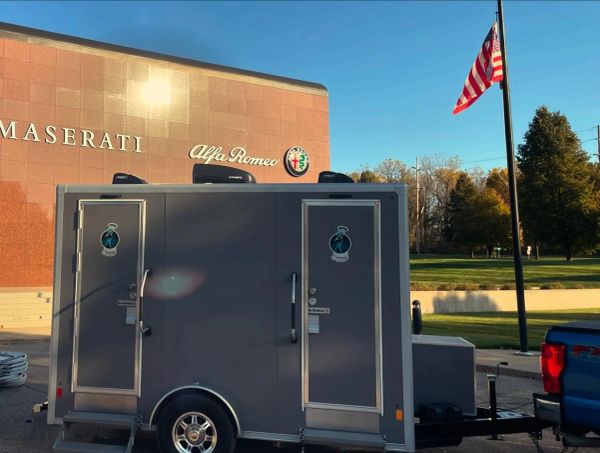 Portable restroom trailer parked outside a Maserati and Alfa Romeo dealership.