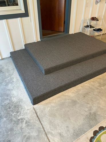 Carpeted two-step porch leading to a wooden door with shoe rack nearby.