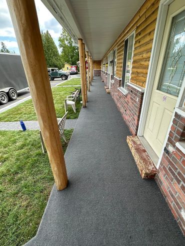 A long porch with wooden pillars and chairs beside a log cabin style building.