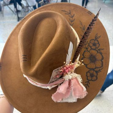 Brown felt hat with floral designs, feathers, and fabric ribbons.