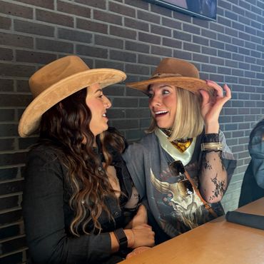 Two women wearing hats share a joyful moment at a table.