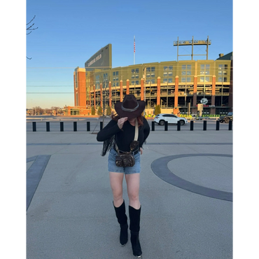 Person in cowboy boots and hat posing in front of Lambeau Field stadium.