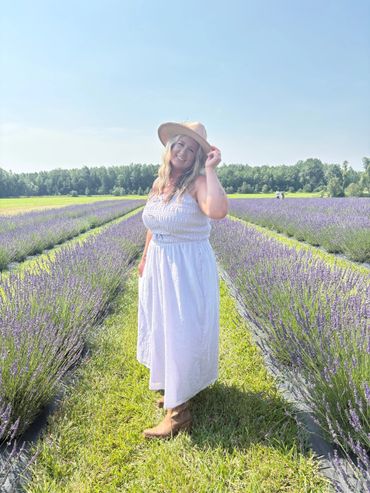 Woman in white dress and hat standing in a blooming lavender field under clear blue sky.