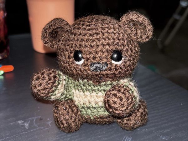 Crocheted brown teddy bear with green-striped sweater.