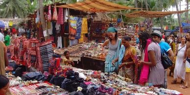 People shopping at an outdoor market with colorful textiles and jewelry.