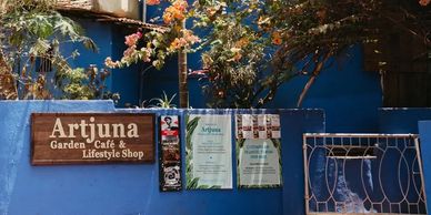 Artjuna Garden Café & Lifestyle Shop entrance with blue walls and vibrant plants.