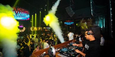 DJ performing live at a vibrant nightclub with colorful lights and smoke effects.