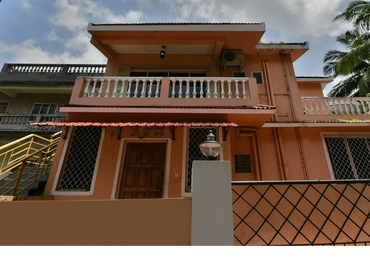 A peach-colored two-story house with a balcony and metal grills on windows.