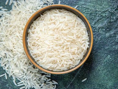 A bowl filled with uncooked white rice on a textured surface.