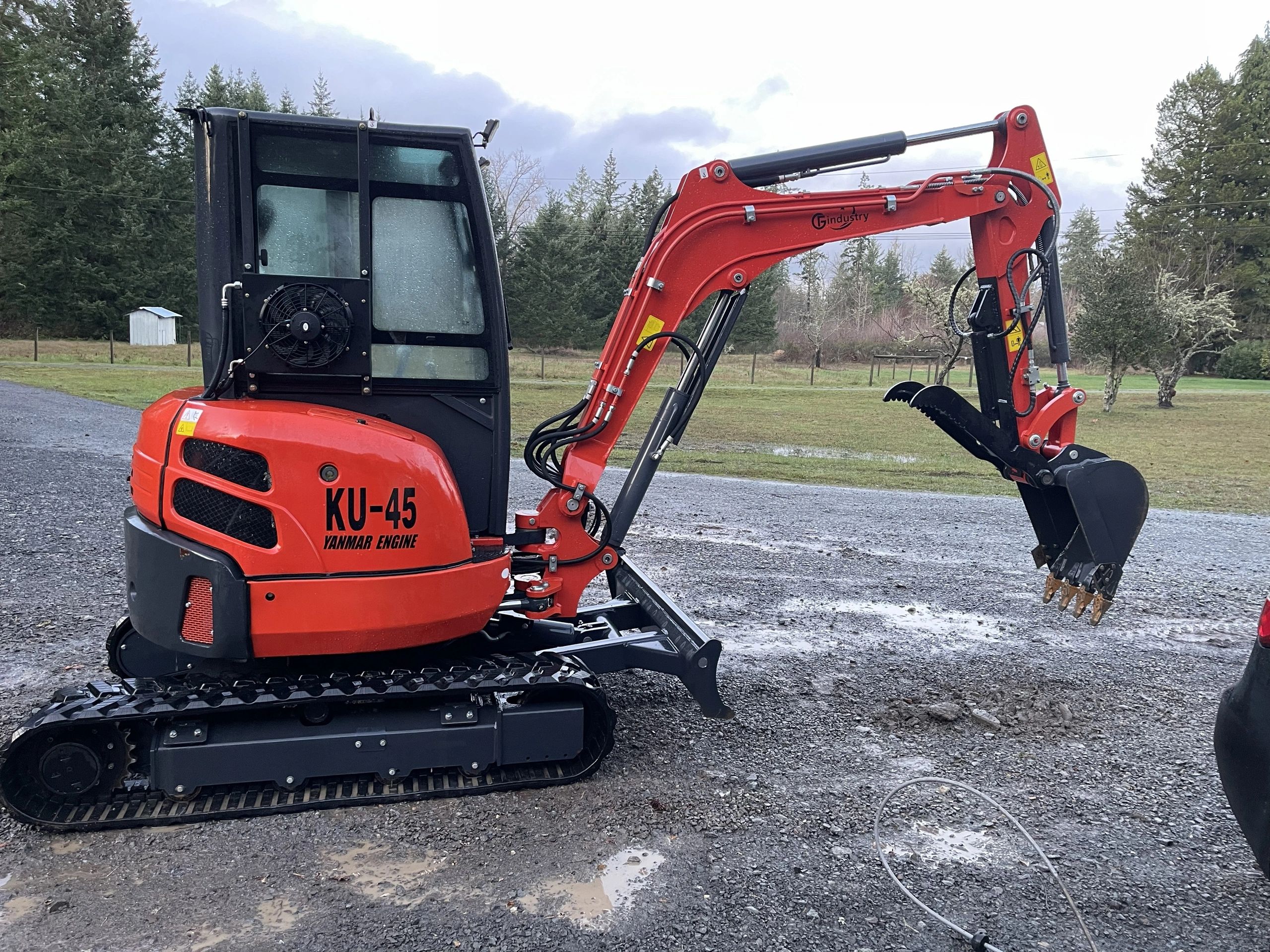 Red compact excavator on gravel surface in a rural setting.