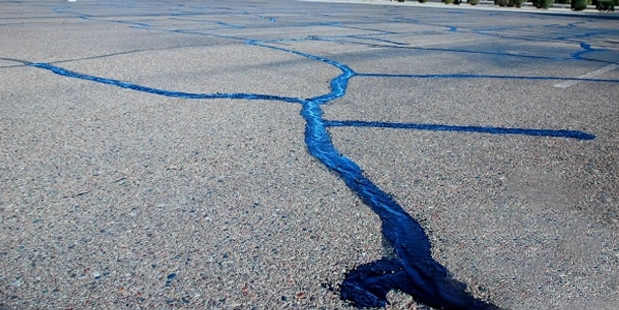 Blue sealant filling cracks on a paved road surface.